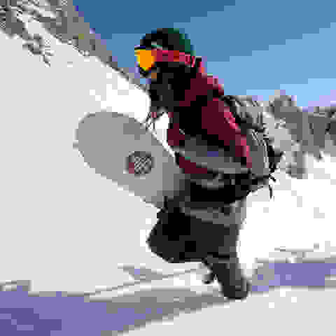 Zwei Snowboarder steigen einen unberührten Tiefschneehang hinauf.