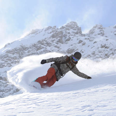 Ein Snowboarder fährt im Tiefschnee durchs Gelände.