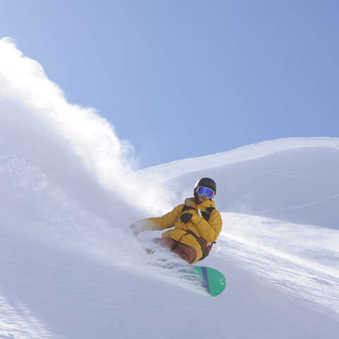 Ein Snowboarder fährt einen unberührten Tiefschneehang hinab.