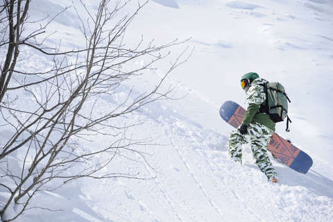 Ein Snowboarder steigt einen unberührten Tiefschneehang hinauf.