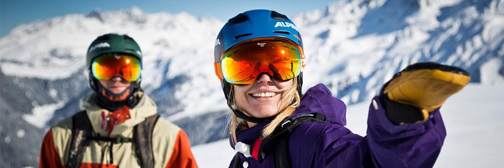 Eine Frau und ein Mann stehen mit Skibrillen und Helmen in einer verschneiten Berglandschaft