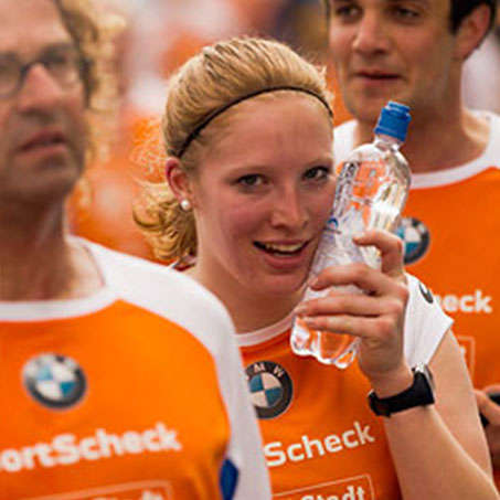 Eine erschöpfte Läuferin presst eine kalte Wasserflasche an ihr Gesicht beim Augsburg SportScheck Stadtlauf.