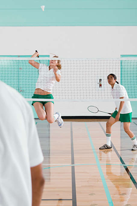 Eine Frau springt während des Badminton Spiels in die Luft, um an den Ball zu gelangen.