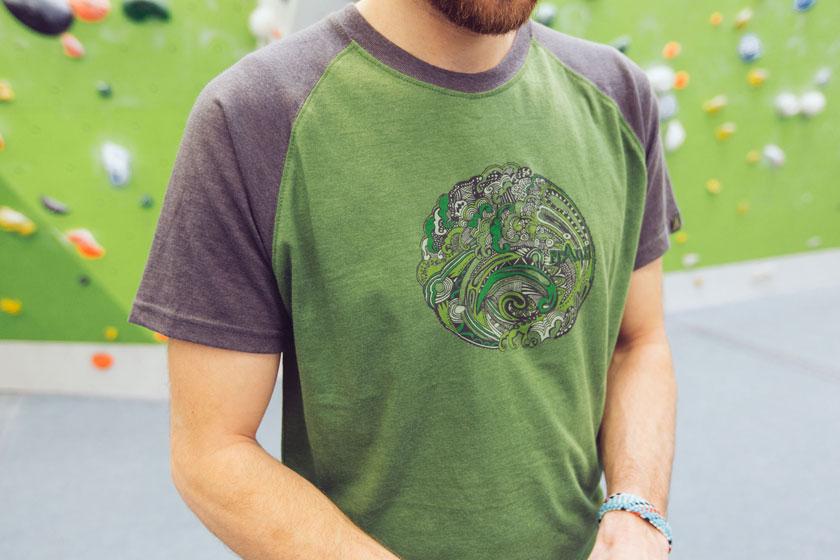 Ein gr&uuml;nes Bouldershirt mit buntem Fantasieaufdruck in der Nahaufnahme.