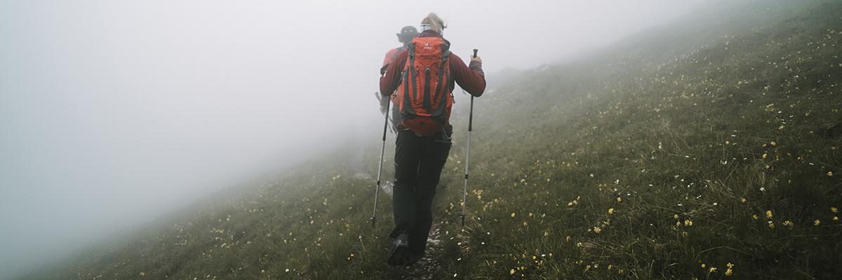 Ein Mann mit langen Haaren wandert mit Wanderstöcken in einem Gebirge.