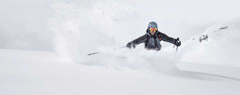 Ein Freeride Skifahrer fährt mit seinen Freeride Ski einen Hang im hüfthohen Tiefschnee hinab