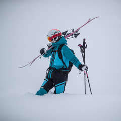Eine Skifahrerin geht mit ihren Ski auf der Schulter und Skistöcken in der Hand ein Stück die Piste hinauf