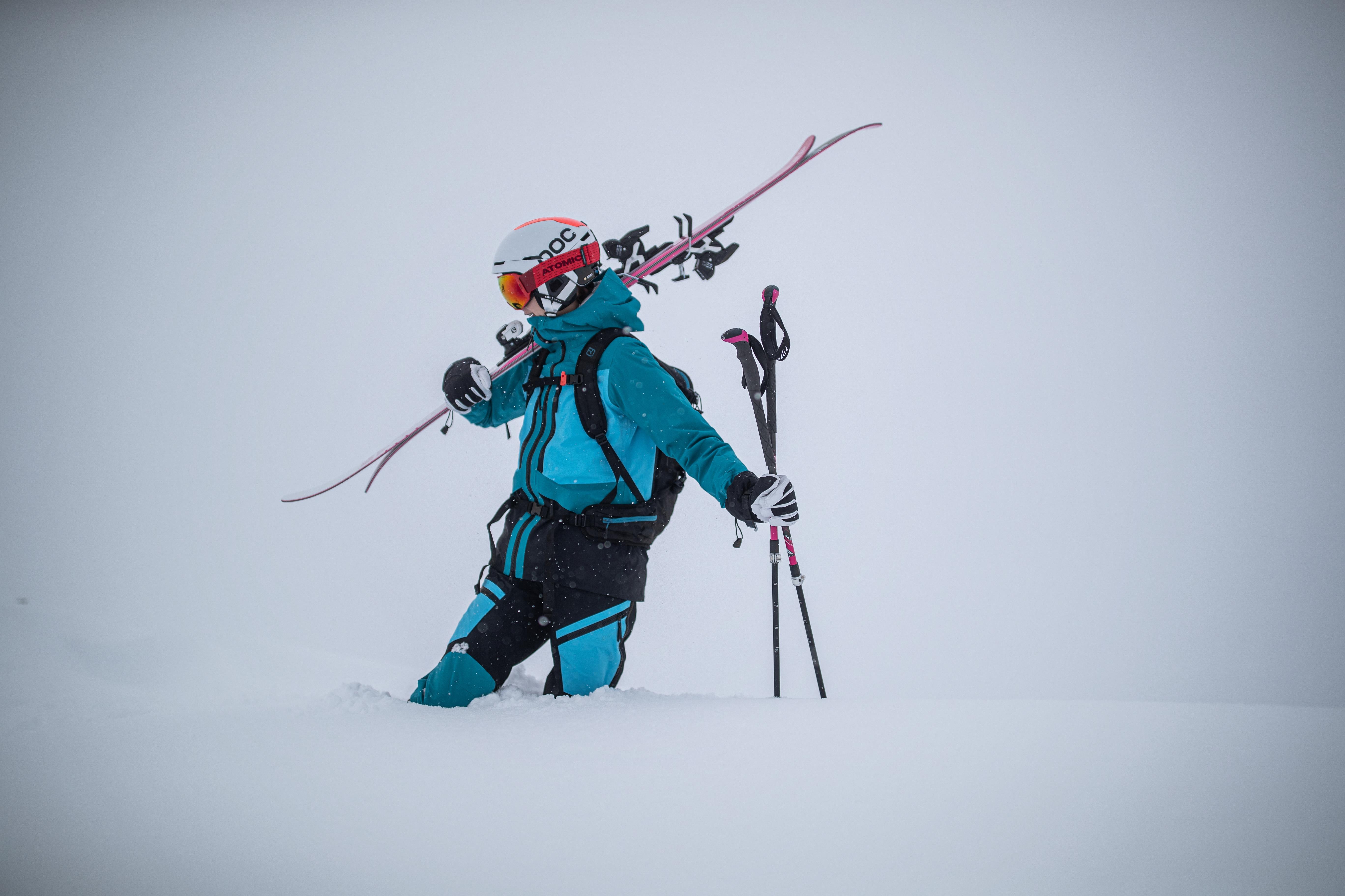 Eine Skifahrerin geht mit ihren Ski auf der Schulter und Skistöcken in der Hand durch kniehohen Tiefschnee.