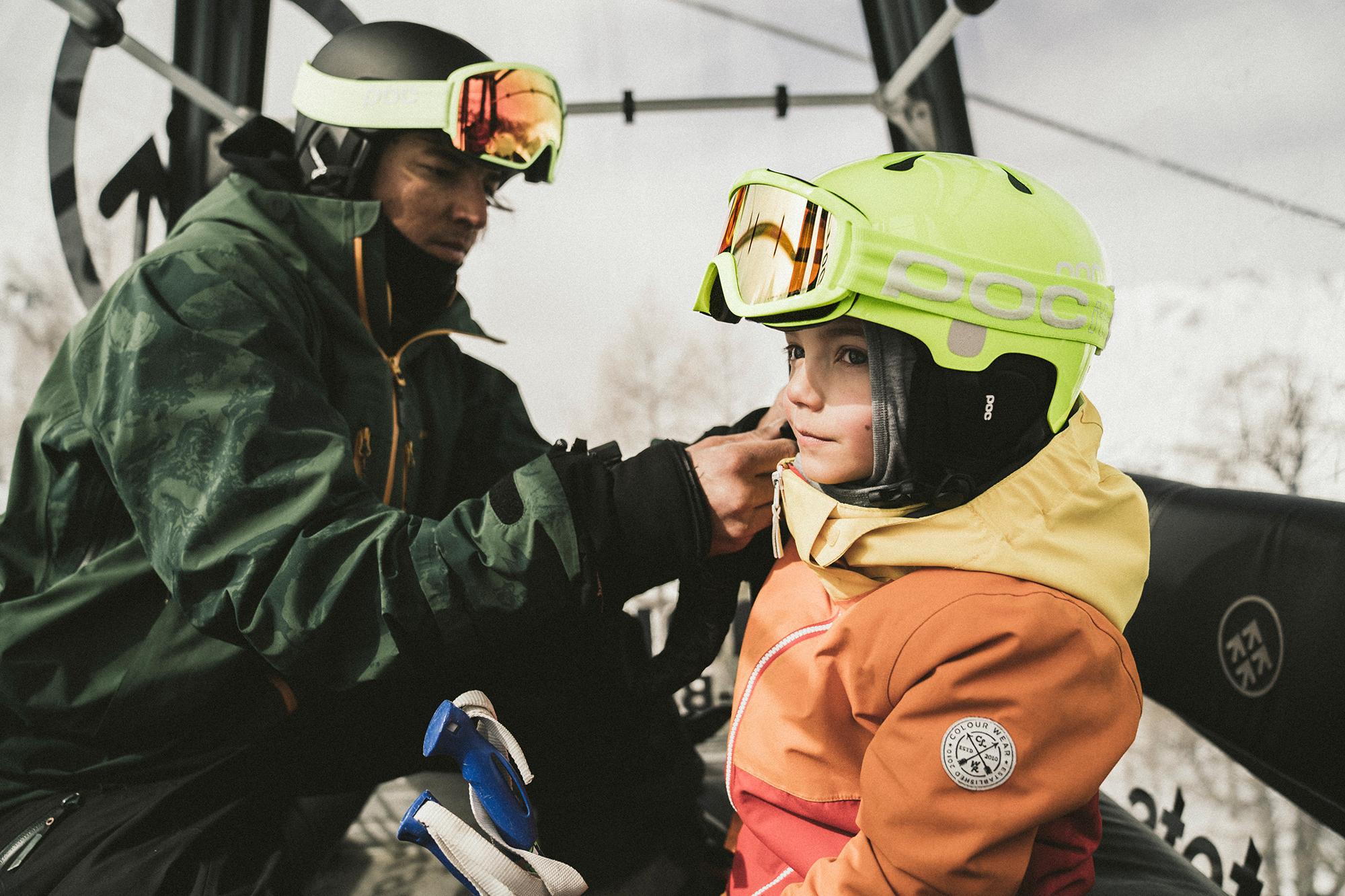 Ein Vater und sein Kind bereiten sich in der Gondel zum Skifahren vor." alt="Ein Vater und sein Kind bereiten sich in der Gondel zum Skifahren vor.