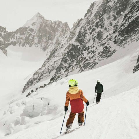 Ein Kind und ein Erwachsener Skifahrer fahren auf Ski eine anspruchsvolle Piste hinab.