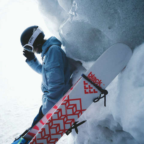 Eine Skitourengeherin lehnt hinter ihren passenden Tourenskiern auf einem Berg. 