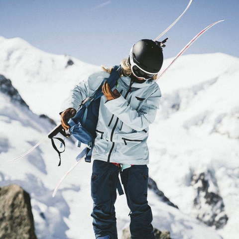 Eine Skitourengeherin setzt sich den Rucksack auf.