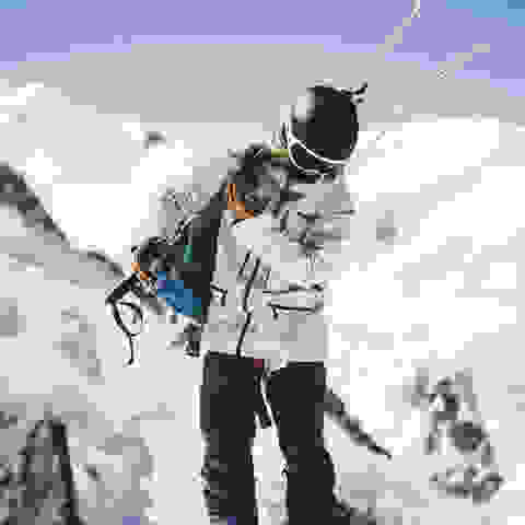 Eine Skitourengeherin setzt sich den Rucksack auf.