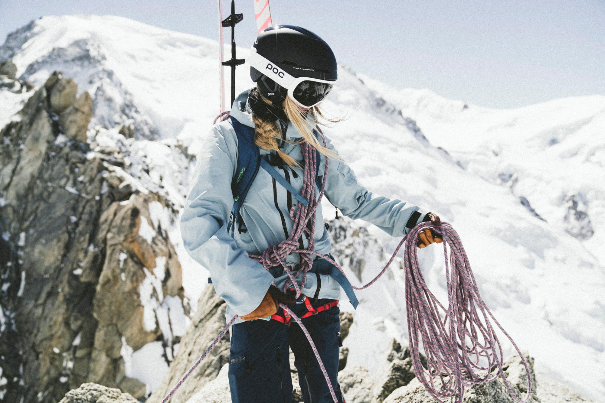 Eine Skitourerin die voll ausgerüstet ist. Sie tragt Skier, Rucksack,Helm. Seil und vieles mehr.