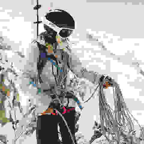 Eine Skitourerin die voll ausgerüstet ist. Sie tragt Skier, Rucksack,Helm. Seil und vieles mehr. 