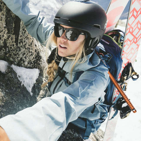 Ein Frau klettert mit einem Helm einen Berg hoch mit ihrer Skiouren Hardware auf dem Rücken. 