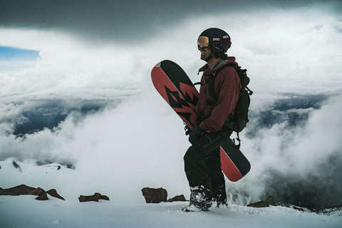 Ein Snowboarder hält sein Splitboard in der Hand während er auf dem Gipfel eines Berges steht.