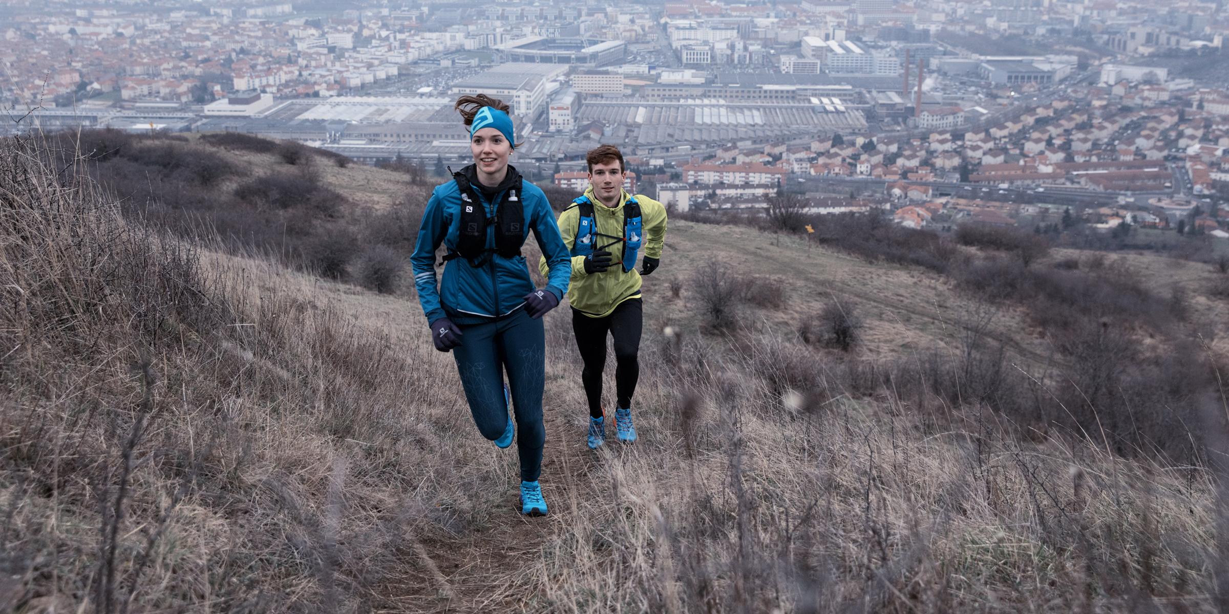 Zwei Trailrunner laufen einen Trail am Rande einer Stadt.