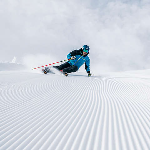 Ein Skifahrer fährt mit Skistöcken in der Hand eine Piste im Carving Schwung hinab