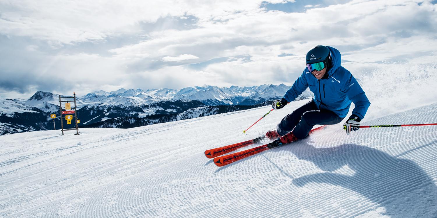 Ein Skifahrer f&auml;hrt mit Skist&ouml;cken in der Hand eine Piste im Carving Schwung hinab