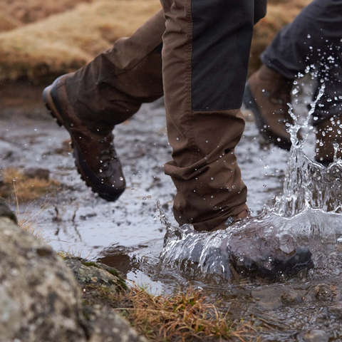 Eine Aufnahme von Füßen die mit Wanderschuhen und Wanderhosen durch ein Flussbett wandern