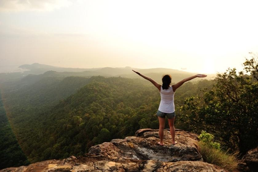 Eine Frau streckt die Arme in einer sonnigen, grünen Berglandschaft nach oben