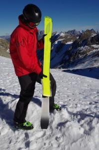 Ein Skifahrer in roter Jacke steht im Schnee und bezieht seinen Tourenski mit Fischer Profoil Skifellen.