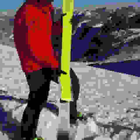 Ein Skifahrer in roter Jacke steht im Schnee und bezieht seinen Tourenski mit Fischer Profoil Skifellen.
