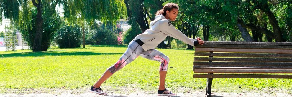 Eine Frau wärmt sich für Ihr Training im Park an einer Bank auf.