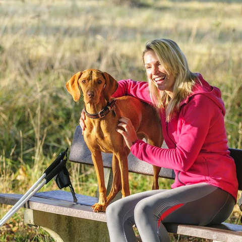 Eine blonde Frau sitzt mit einem braunen Hund auf einer Parkbank.