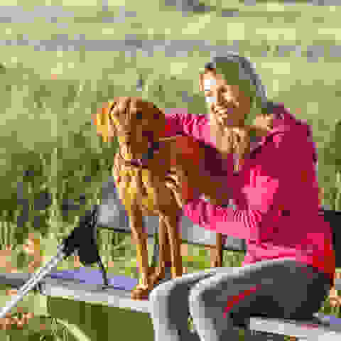 Eine blonde Frau sitzt mit einem braunen Hund auf einer Parkbank.