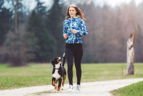 Eine junge Frau joggt mit einem jungen Hund