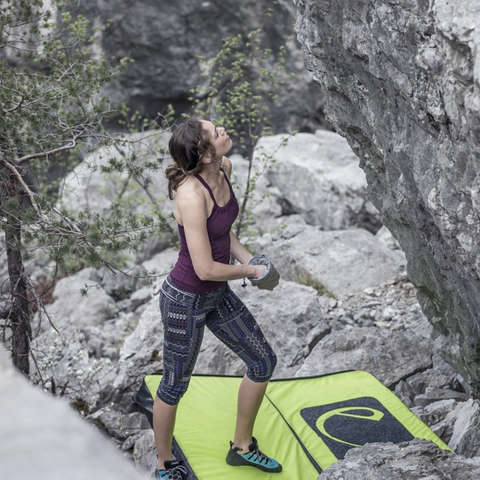Eine Frau steht vor einer Felswand und schaut nach oben. Vor ihr liegt eine Bouldermatte für die Sicherheit.