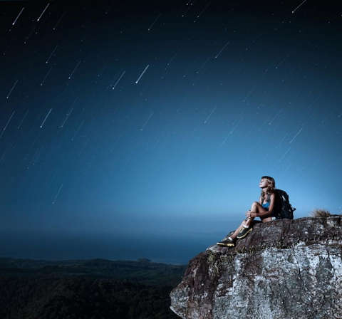 Eine Frau sitzt auf einem Berg und schaut zum Sternenhimmel hinauf.