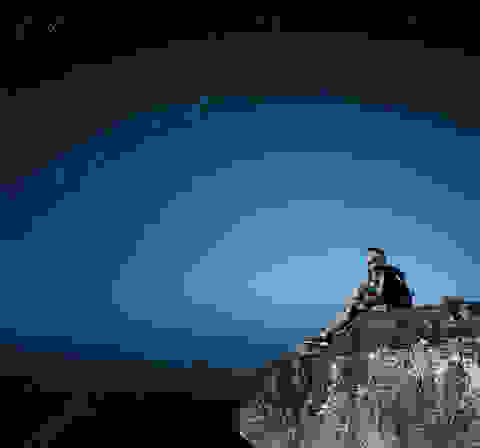 Eine Frau sitzt auf einem Berg und schaut zum Sternenhimmel hinauf.