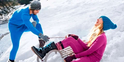 Ein Mann und eine Frau spielen im Schnee in Merinowolle Unterwäsche.