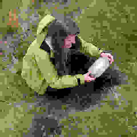 Eine junge Frau verbuddelt beim Geocaching einen Cache. 