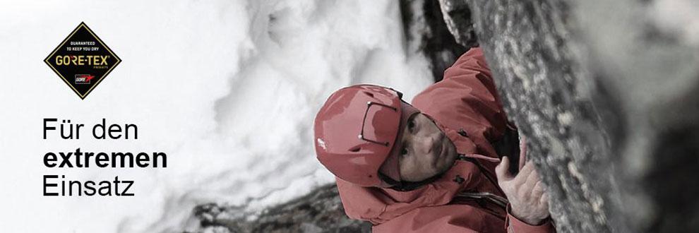 Ein Mann klettert eine Bergwand hinauf. Er tr&auml;gt einen roten Schutzhelm und eine rote Gore Tex Pro Jacke.