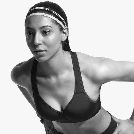Eine Frau steht mit den Händen auf die Hüften gestützt leicht vorgebeugt. Sie trägt einen Nike Sport-Bra in schwarz.
