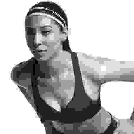 Eine Frau steht mit den Händen auf die Hüften gestützt leicht vorgebeugt. Sie trägt einen Nike Sport-Bra in schwarz.