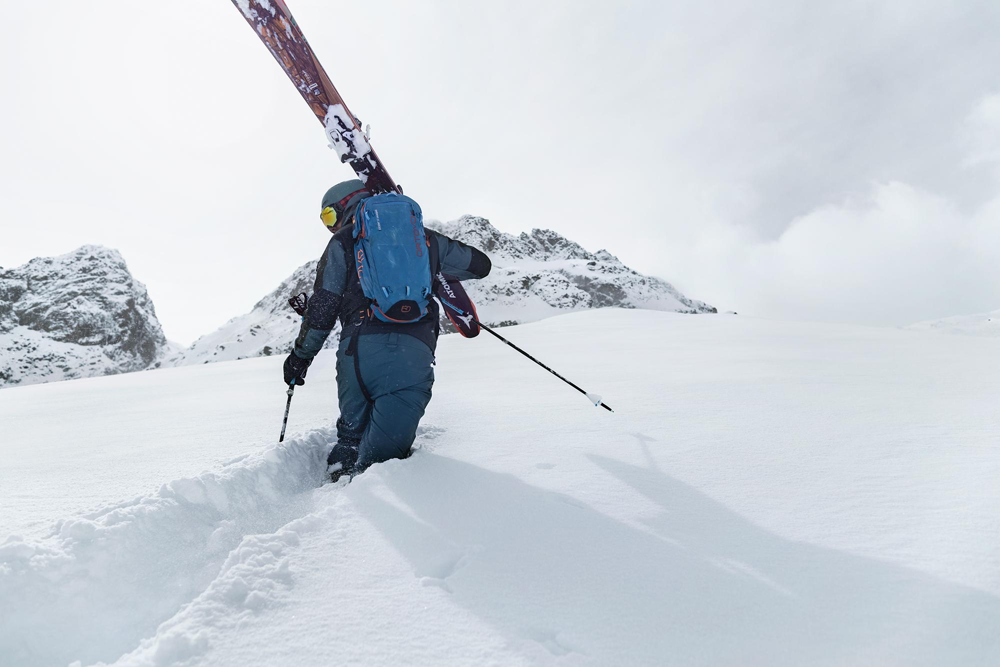 Ein Mann der mit seinen Tourenski in der Hand im Tiefschnee steht