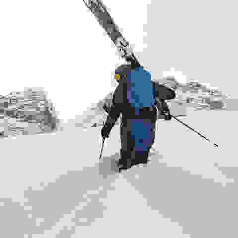 Ein Mann steht mit seiner kompletten Skitourenausrüstung im Tiefschnee.