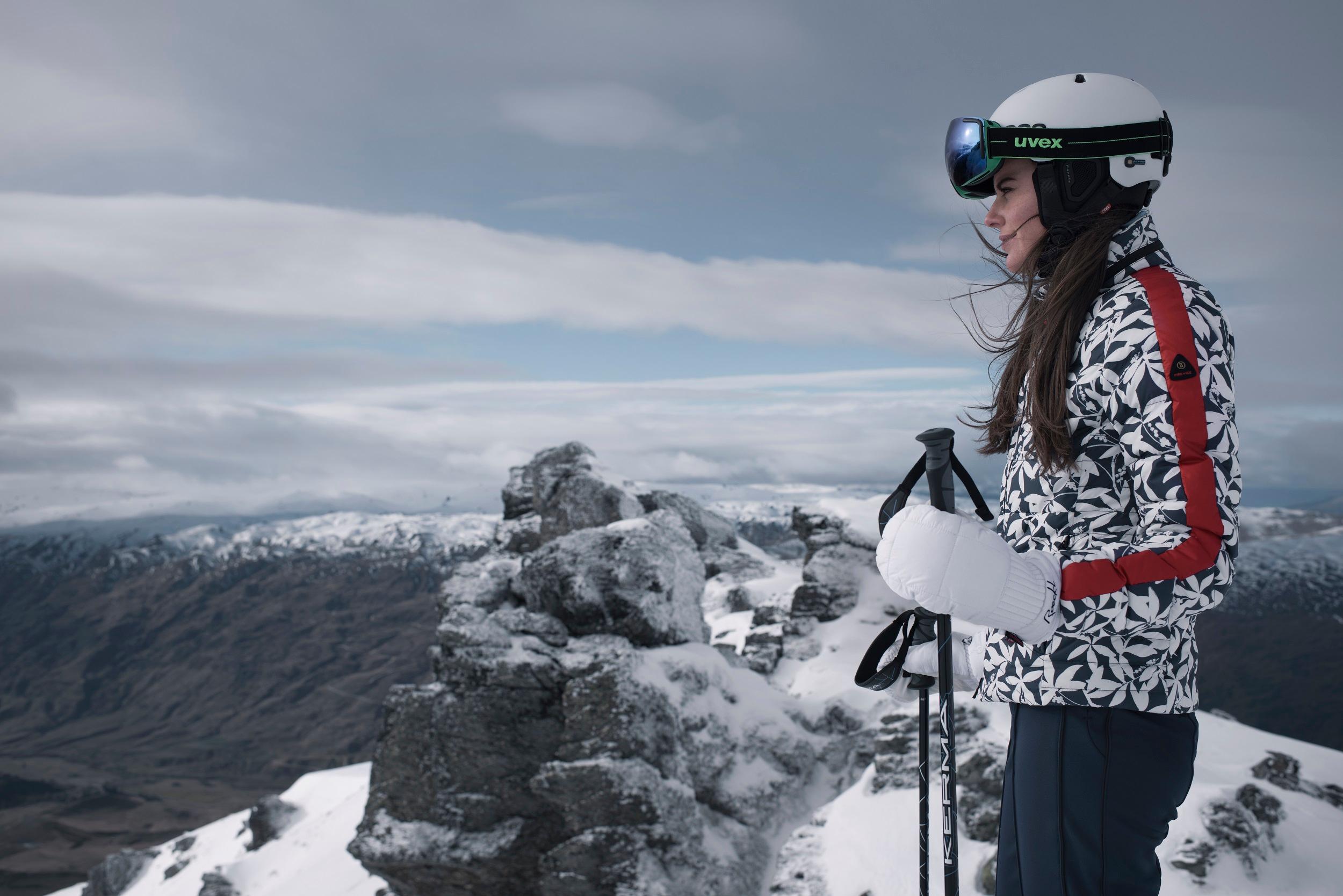 Eine Skifahrerin steht in voller Skibekleidung auf dem Gipfel eines Berges" alt="Eine Skifahrerin steht in voller Skibekleidung auf dem Gipfel eines Berges