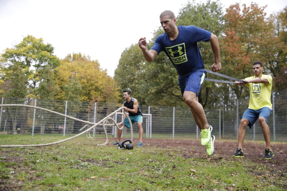 3 M&auml;nner machen Partner&uuml;bungen auf einem Rasenplatz.