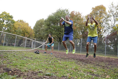 Drei Männer trainieren mit ihrem Körpergewicht auf einem Rasenplatz.
