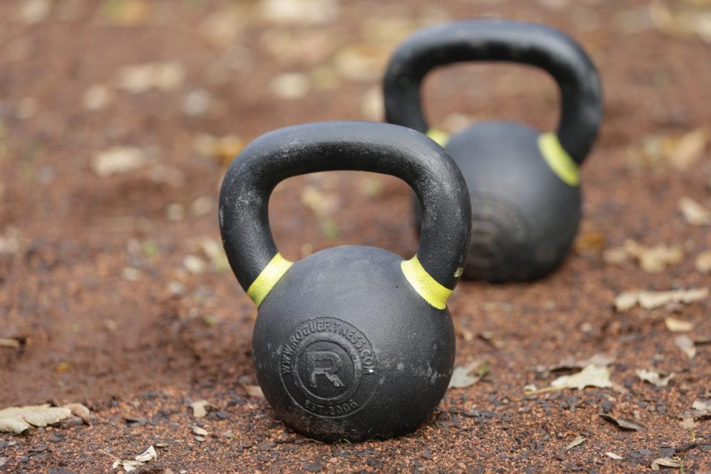 Zwei Kettlebells auf sandigem Untergrund.