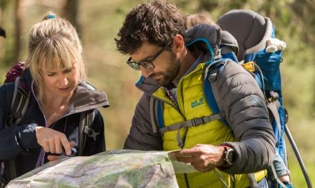 Ein Mann kümmert sich um eine Frau die sich beim Wandern das Knie verletzt hat