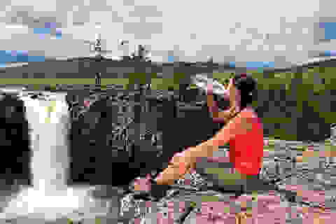 Eine Frau sitzt auf einem Berg und trinkt aus einer Wasserflasche.