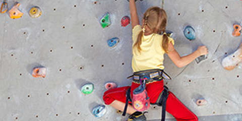 Ein Mädchen bouldert in einer Kletterhalle mit entsprechenden Kletterschuhen für Kinder.
