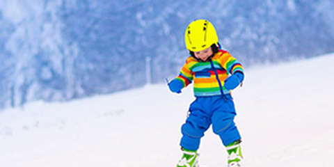 Ein kleines Kinder fährt in Skischuhen und Skiern eine Piste hinab.